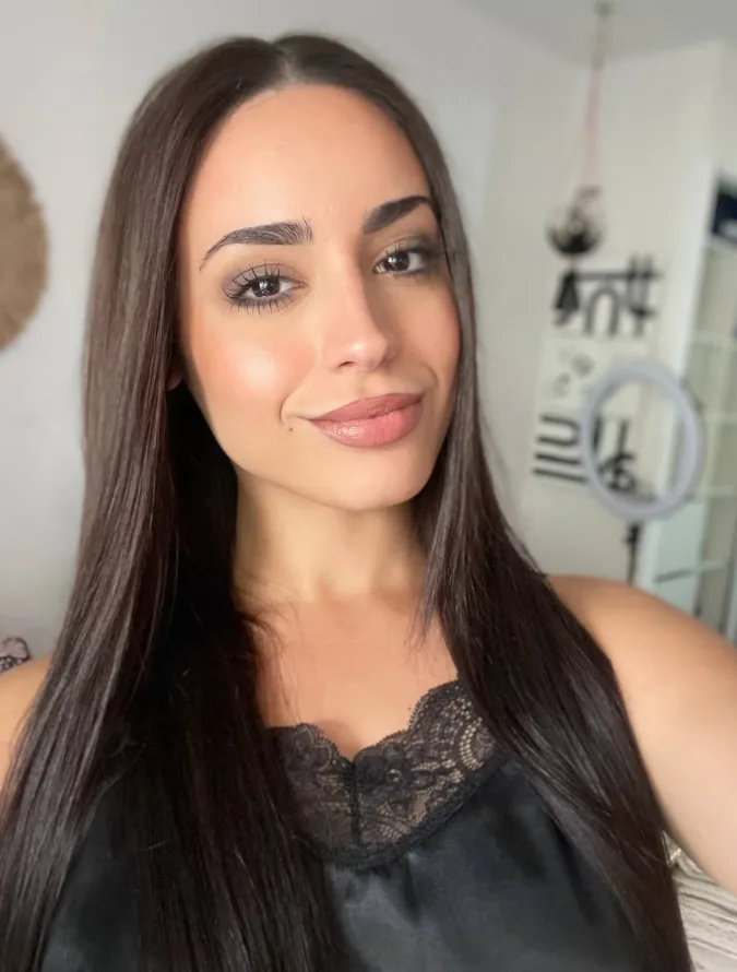 Close-up portrait of a woman with long dark hair wearing a black lace-trim top, smiling softly at the camera.