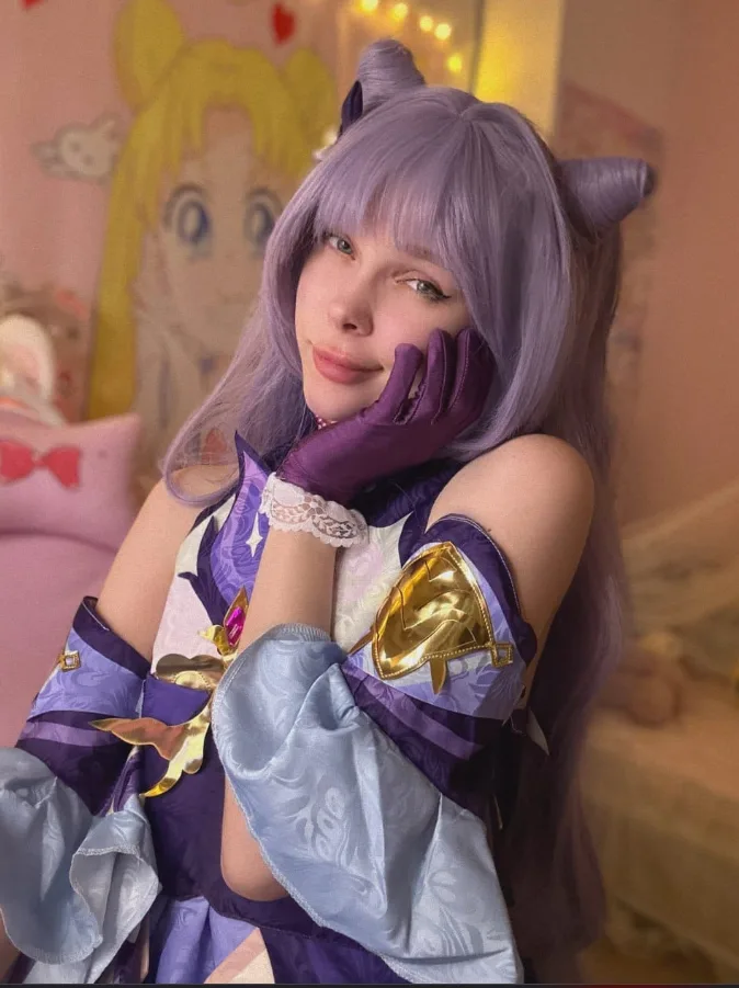 Cosplayer with lavender wig and cat ears posing with hand on cheek in a purple/lavender costume.