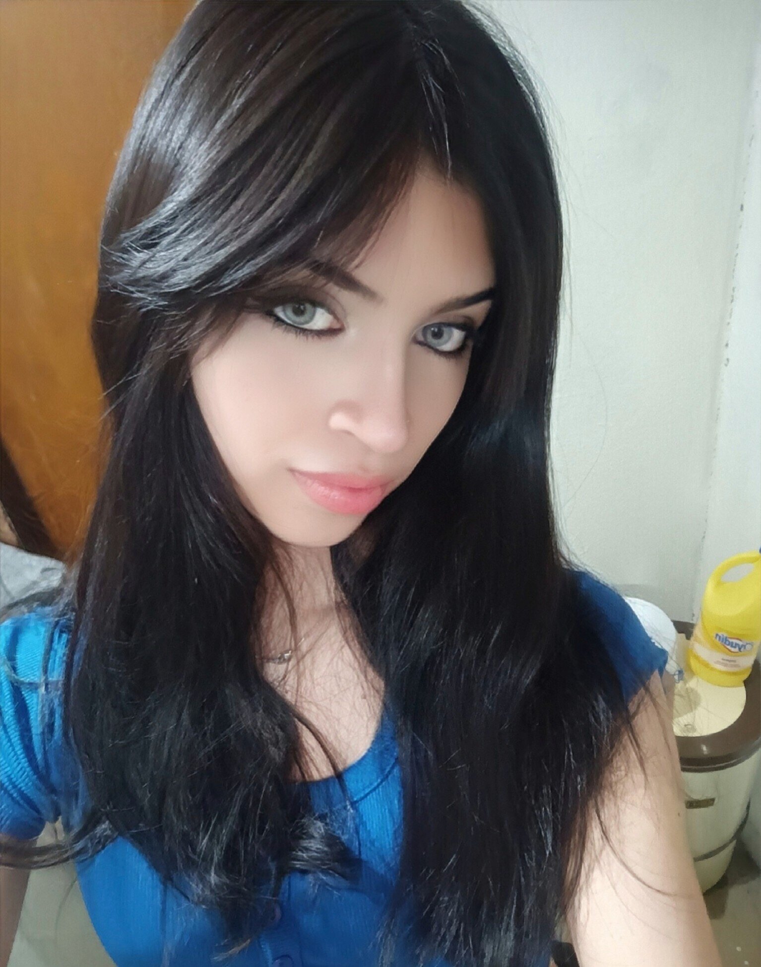 Close-up of a young woman with long dark hair and blue eyes, wearing a blue top, looking at the camera.